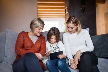 Ein kleines Mädchen mit Tablet und ihre Mutter und Großmutter zu Hause. Familie und Generationen Konzept. - HPIF19815