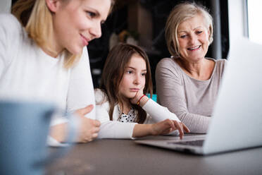 Ein kleines Mädchen mit Laptop und ihre Mutter und Großmutter zu Hause. Familie und Generationen Konzept. - HPIF19821