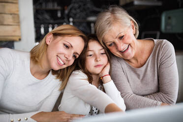 Ein kleines Mädchen mit Laptop und ihre Mutter und Großmutter zu Hause. Familie und Generationen Konzept. - HPIF19822