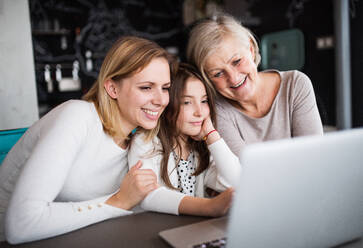 Ein kleines Mädchen mit Laptop und ihre Mutter und Großmutter zu Hause. Familie und Generationen Konzept. - HPIF19823