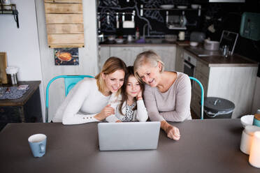 A small girl with laptop and her mother and grandmother at home. Family and generations concept. - HPIF19824