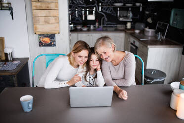 Ein kleines Mädchen mit Laptop und ihre Mutter und Großmutter zu Hause. Familie und Generationen Konzept. - HPIF19824