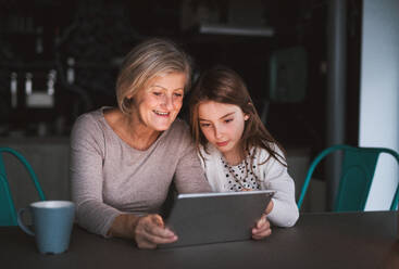 Ein kleines Mädchen und ihre Großmutter mit einem Tablet zu Hause. Familien- und Generationenkonzept. - HPIF19828
