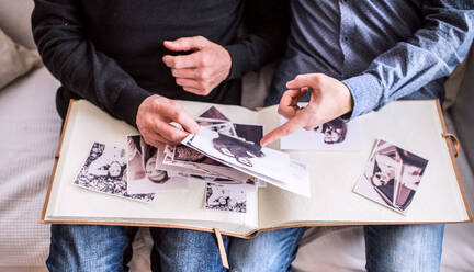 Unrecognizable son and his senior father at home, looking at old photographs. Two generations indoors. - HPIF19856