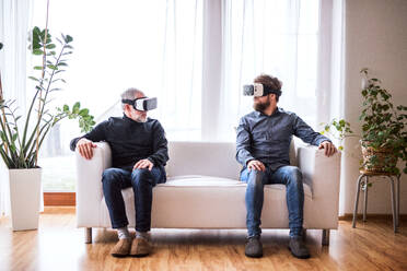 Hipster son and his senior father with VR goggles at home. Two generations indoors, having fun. - HPIF19868