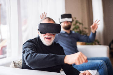 Hipster son and his senior father with VR goggles at home. Two generations indoors, having fun. - HPIF19869