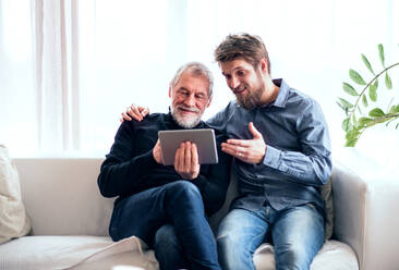 Hipster-Sohn und sein älterer Vater mit Tablet zu Hause: Zwei Generationen in einem Haus, die Spaß haben. - HPIF19875