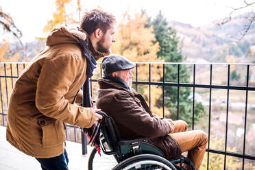 Ein Vater im Rollstuhl und sein kleiner Sohn gehen spazieren, ein Pfleger hilft einem behinderten älteren Mann. - HPIF19891