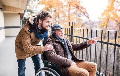 Ein Vater im Rollstuhl und sein kleiner Sohn gehen spazieren, ein Pfleger hilft einem behinderten älteren Mann. - HPIF19892