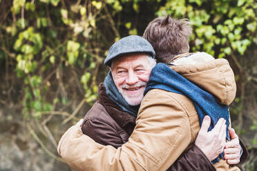 Ein älterer Vater und sein kleiner Sohn umarmen sich bei einem Spaziergang in der Stadt. - HPIF19894