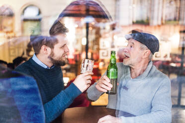 Älterer Vater und sein junger Sohn trinken Bier in einer Kneipe, Aufnahme durch Glas. - HPIF19904