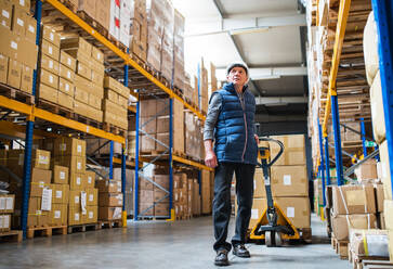 Senior male warehouse worker pulling a pallet truck with boxes. - HPIF19921