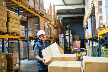 Senior male warehouse worker loading or unloading boxes from a pallet truck. - HPIF19925