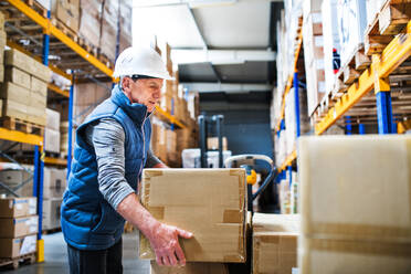 Senior male warehouse worker loading or unloading boxes from a pallet truck. - HPIF19927