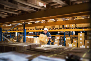 Senior male warehouse worker or a supervisor with white helmet loading or unloading a pallet truck with boxes. - HPIF19930