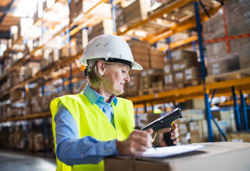 Senior warehouse woman worker or supervisor using a mobile handheld PC with barcode scanner. - HPIF19949