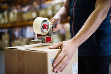 Unrecognizable male warehouse worker or a supercisor sealing cardboard boxes. - HPIF19995