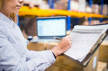 Unrecognizable young woman warehouse worker or supervisor with clipboard, controlling stock. - HPIF20082