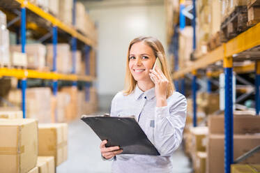 Young woman warehouse worker or supervisor with smartphone, making a phone call. - HPIF20084