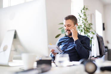 Geschäftsmann im Rollstuhl mit Smartphone am Schreibtisch im Büro, der einen Anruf tätigt. - HPIF20105