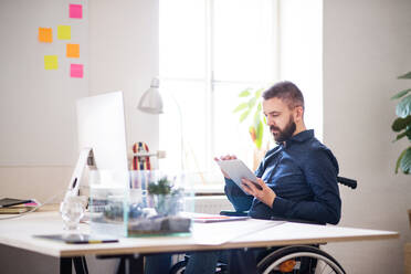 Geschäftsmann im Rollstuhl mit Tablet am Schreibtisch im Büro, arbeiten. - HPIF20107