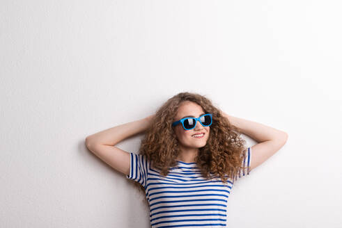 Junge, schöne, fröhliche Frau mit blauer Sonnenbrille im Studio, die Hände hinter dem Kopf. - HPIF20122