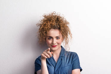 Young beautiful happy woman standing in studio, looking at camera and finger pointing at you. - HPIF20126