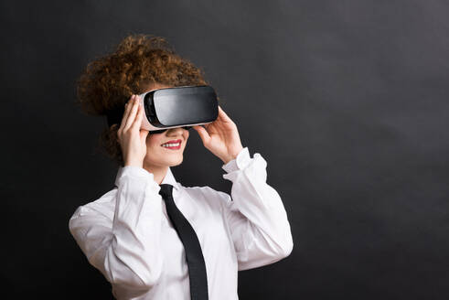 Porträt einer jungen schönen Frau mit Virtual-Reality-Brille in einem Studio, mit weißem Hemd und schwarzer Krawatte. - HPIF20127