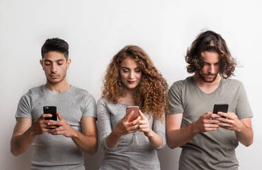 A portrait of young occupied girl with two boy friends standing in a studio, using smartphone. - HPIF20132