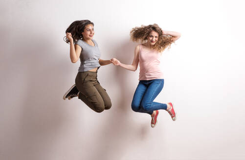 Zwei junge, schöne, fröhliche Frauen im Studio, die sich an den Händen halten und springen. - HPIF20133