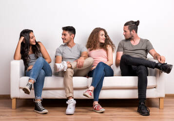 Porträt einer jungen Gruppe fröhlicher Freunde, die auf einem Sofa in einem Studio sitzen und sich unterhalten. - HPIF20135
