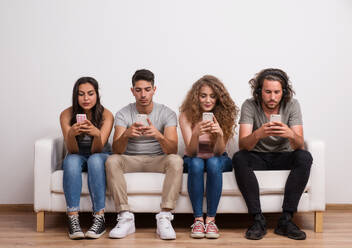 A young group of friends sitting on a sofa in a studio, using smartphones. - HPIF20136