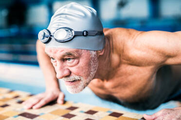 Älterer Mann steht am Hallenbad und dehnt sich. Aktiver Rentner beim Sport. - HPIF20159