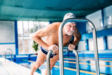 Älterer Mann steht am Hallenbad und dehnt sich. Aktiver Rentner beim Sport. - HPIF20161