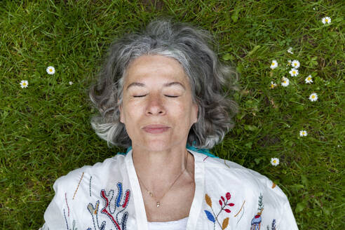 Ältere Frau mit geschlossenen Augen auf grünem Gras liegend - FLLF00890