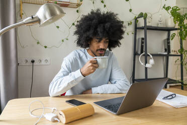 Freelancer having coffee with laptop on desk at home - VPIF08150