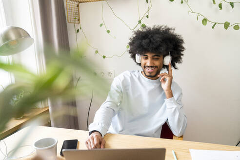 Smiling freelancer adjusting headphones at home - VPIF08154