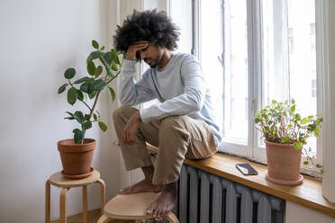 Man with head in hand sitting on window sill at home - VPIF08184