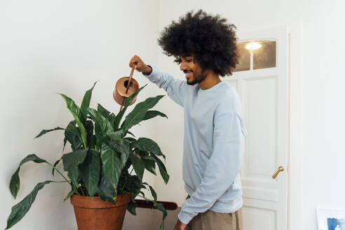 Smiling man watering plants at home - VPIF08192