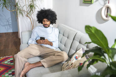 Mann, der ein Smartphone benutzt, sitzt auf dem Sofa zu Hause - VPIF08199