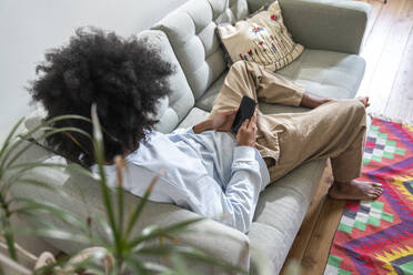 Mann benutzt Smartphone und entspannt sich auf dem Sofa zu Hause - VPIF08201