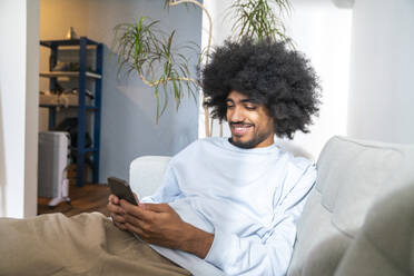 Lächelnder Mann mit lockigem Haar, der zu Hause ein Mobiltelefon benutzt - VPIF08202