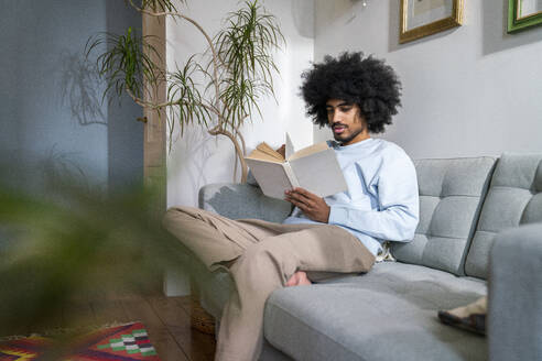 Man reading book sitting on sofa at home - VPIF08207