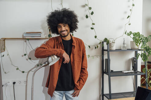 Smiling man leaning on desk lamp at home - VPIF08243