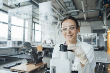 Smiling young scientist with microscope seen through glass - JOSEF19550