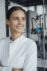 Happy young scientist standing in front of glass cabinet - JOSEF19559