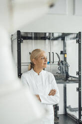 Thoughtful scientist standing with arms crossed in front of cabinet - JOSEF19596