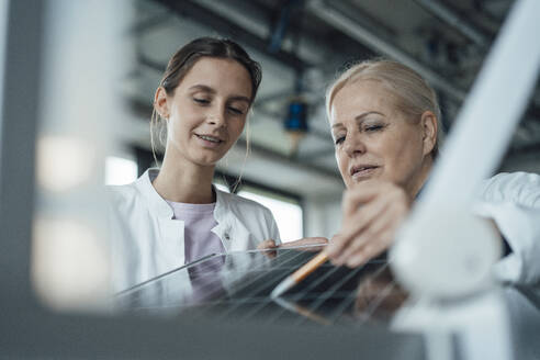 Smiling scientist with colleague discussing over solar panel - JOSEF19597