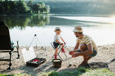 A mature father with a small toddler son outdoors fishing by a river or a lake. - HPIF20185