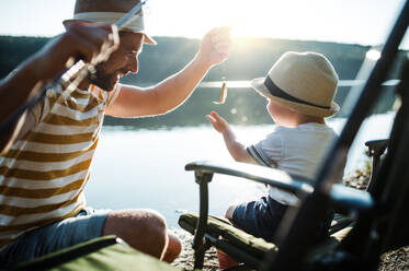 A mature father with a small toddler son outdoors fishing by a river or a lake. - HPIF20189